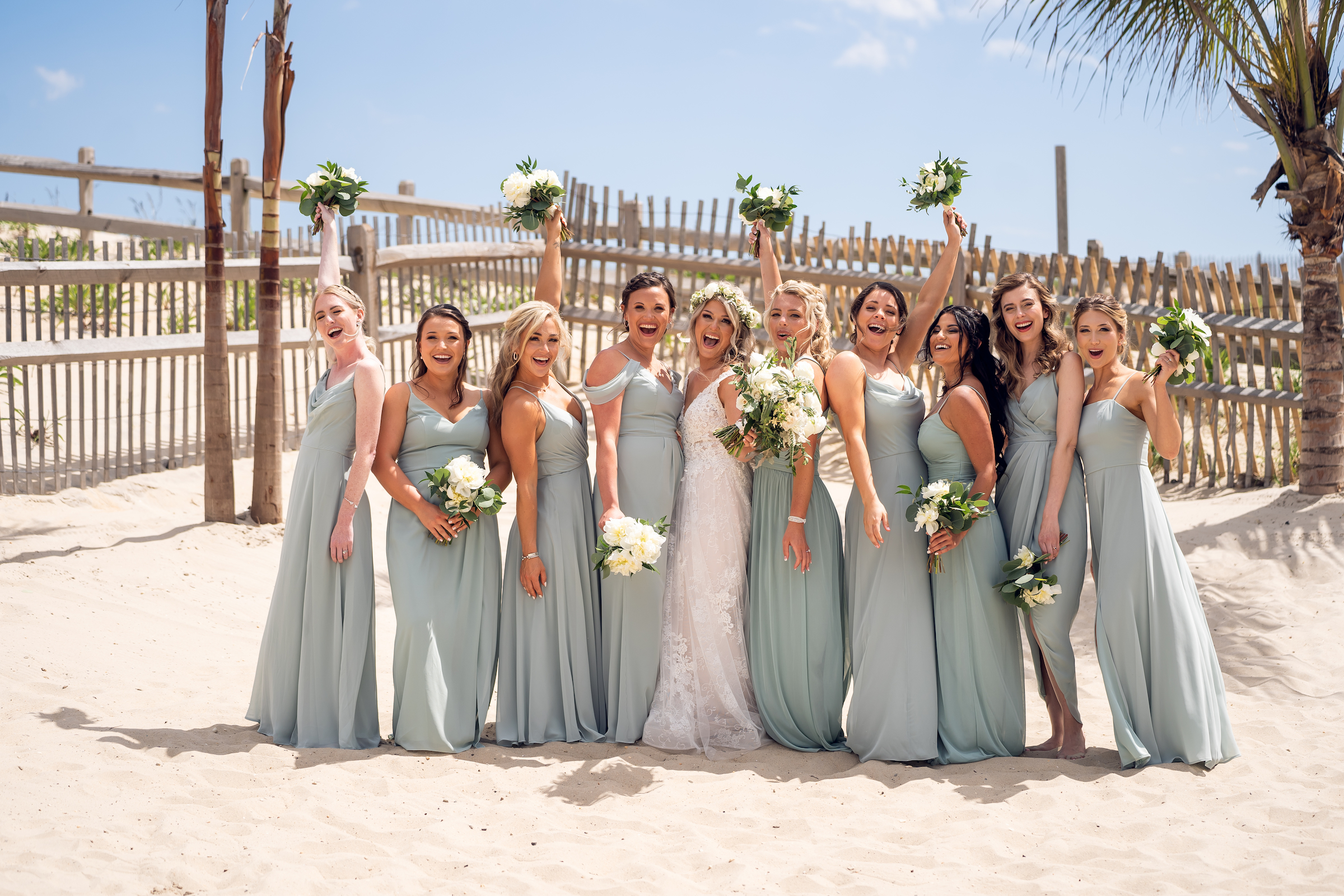 The bride is flanked her her bridesmaids in sage green dresses on the beach for the Sea Shell Resort and Beach Club wedding.