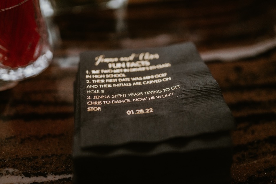A black napkin with gold lettering features fun facts about the couple.
