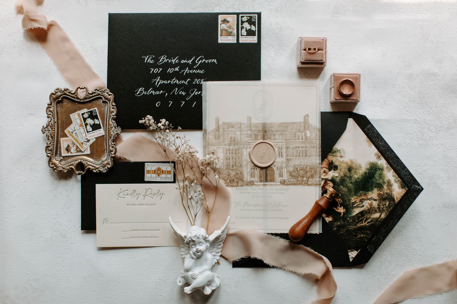 A close up of the invitations, stamps, rings and some baby's breath and a small white cherub figurine.