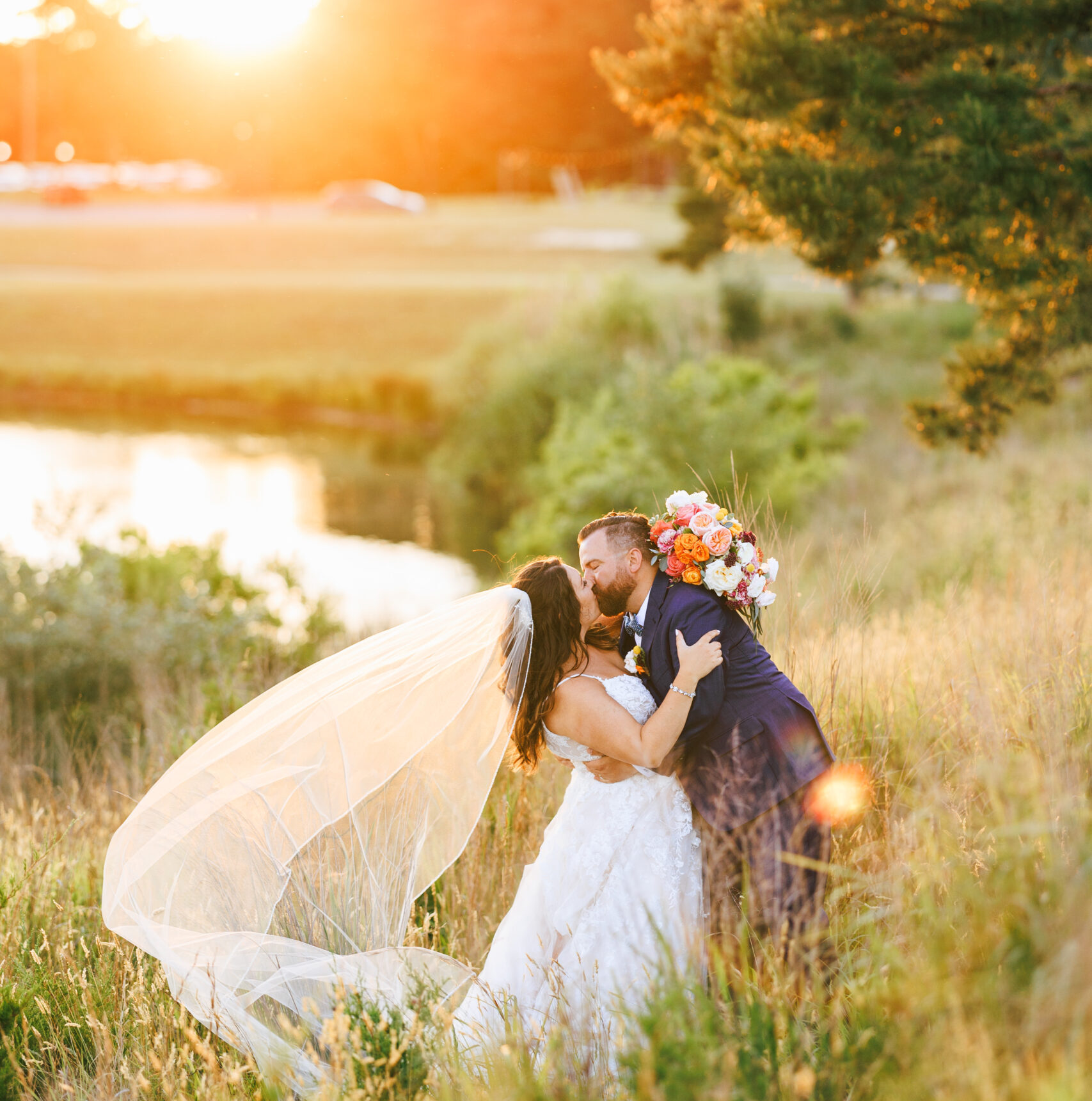 The couple kisses as the bride's veil blows in the wind with the sunsetting the background at their Renault Winery wedding.