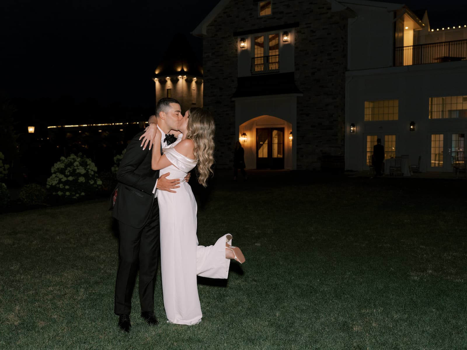 Outside at night the couple kiss and embrace. The bride pops her foot.