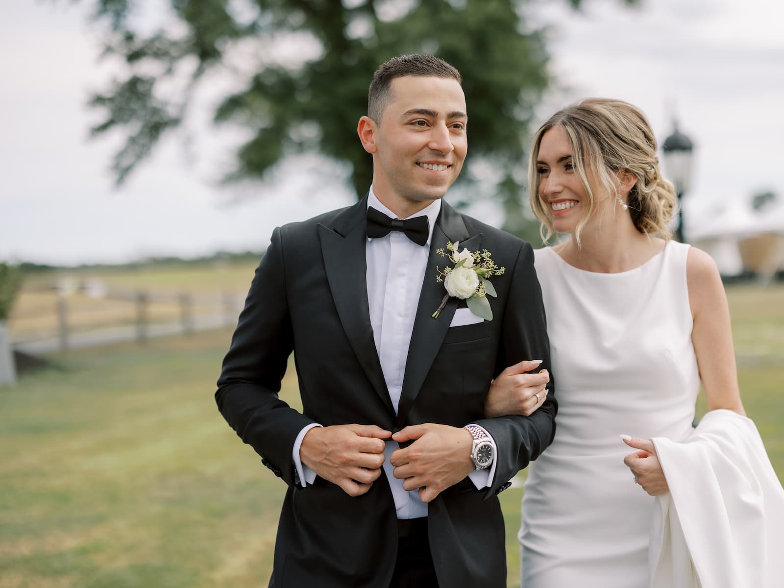 At their Renault Wintery wedding, the groom and bride smile as they link arms and walk on the grounds of the property.