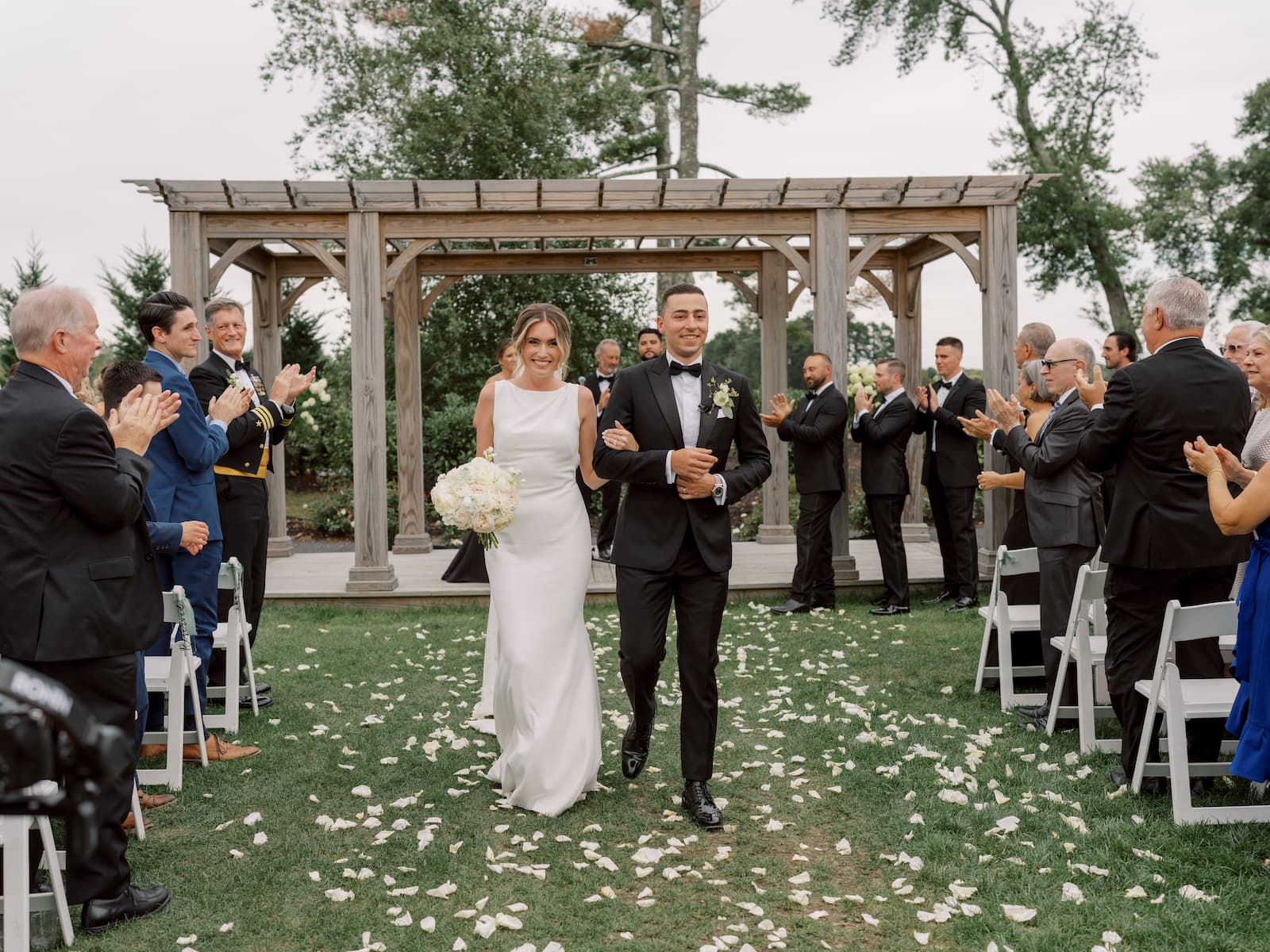 The bride and groom exit their outdoor ceremony with a large wooden archway behind them.