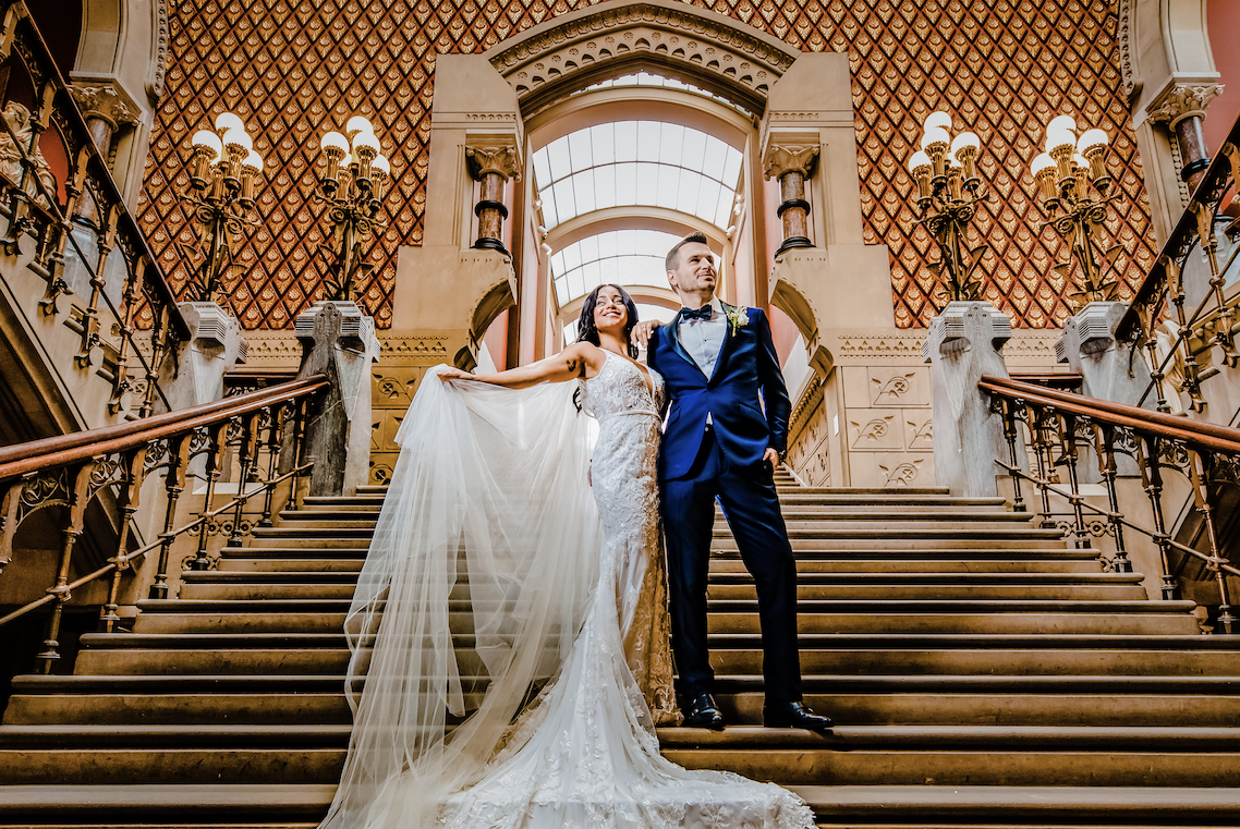 Wondering what to know when hiring an NJ wedding photographer to capture your special day? Read more. Pictured here, a bride and groom stand on a grand staircase.
