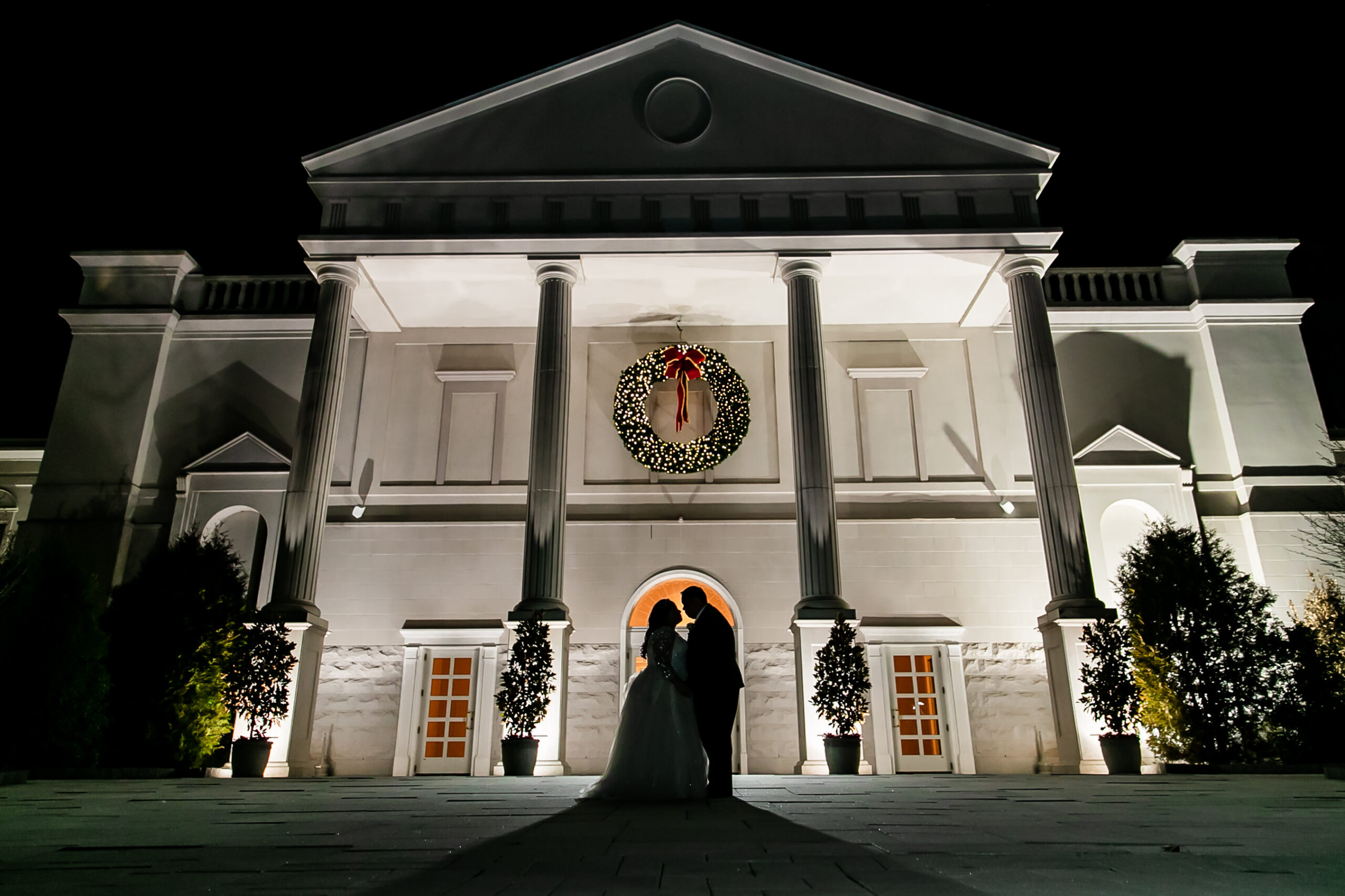 The coupe takes a silhouette photo outside the venue at night with a big Christmas wreath on the building.