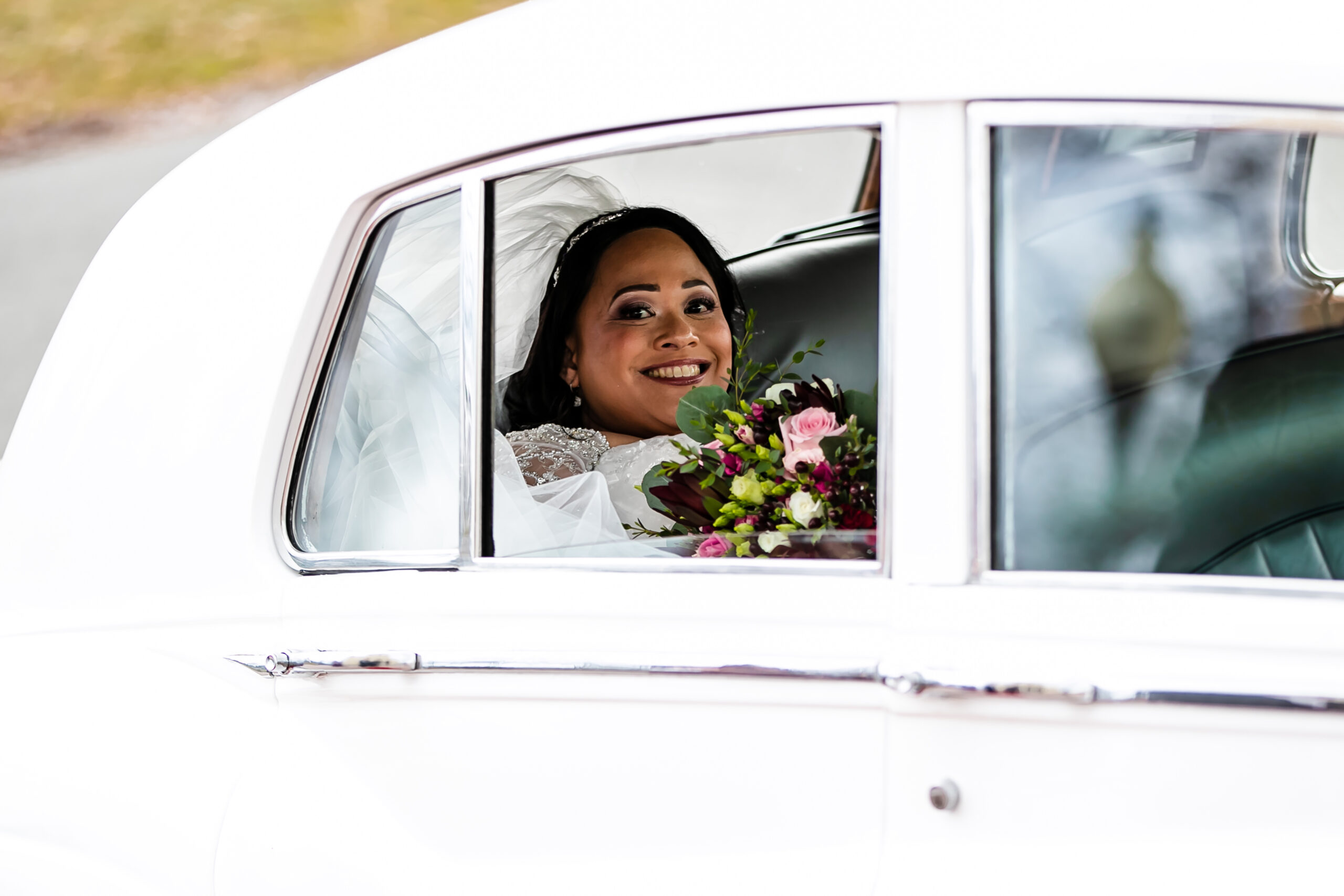 The bride smiles bug from inside a white vintage car before her Palace at Somerset Park wedding.