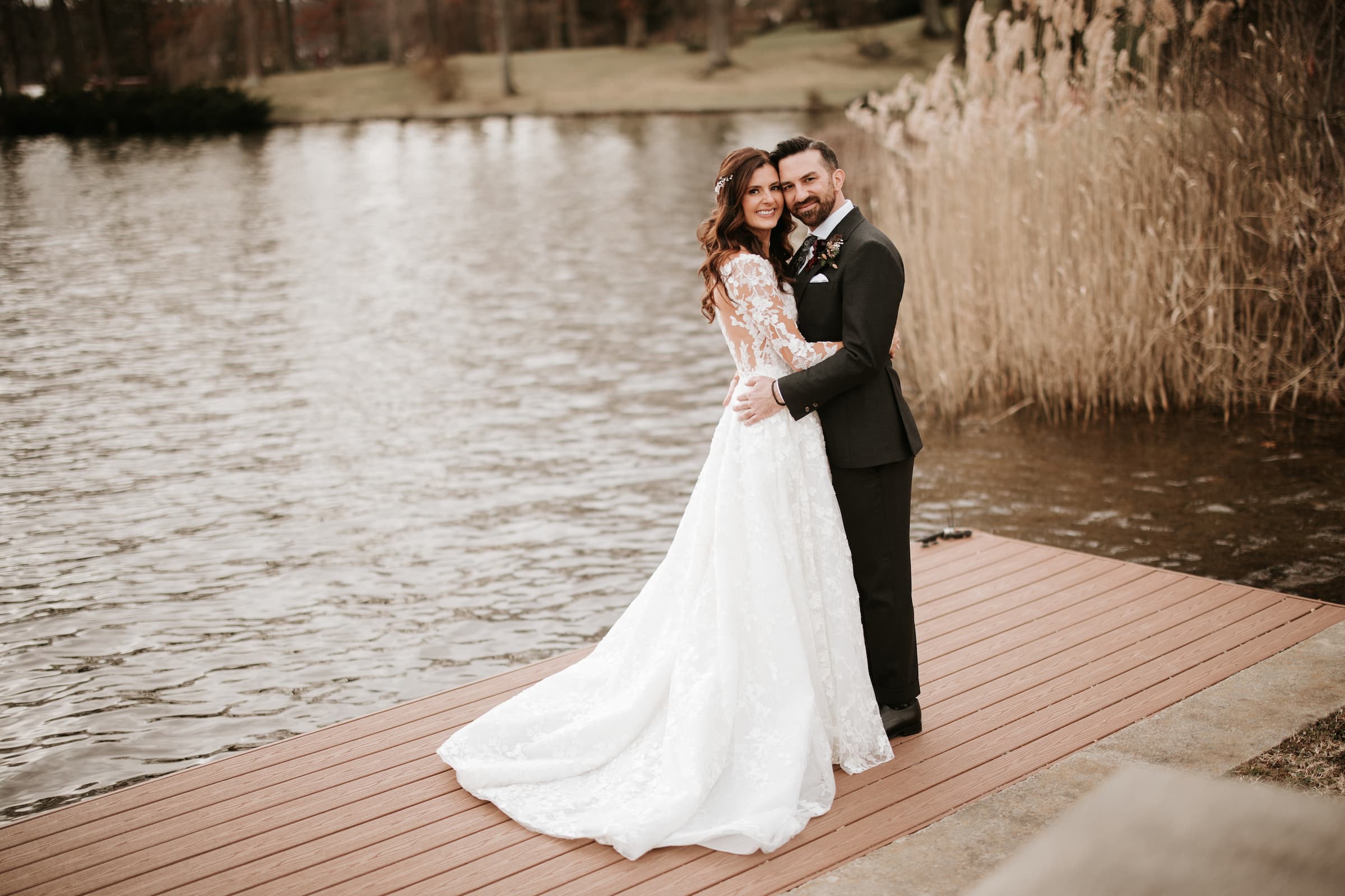 A portrait of the bride and groom embracing but looking at the camera with a lake in the background.