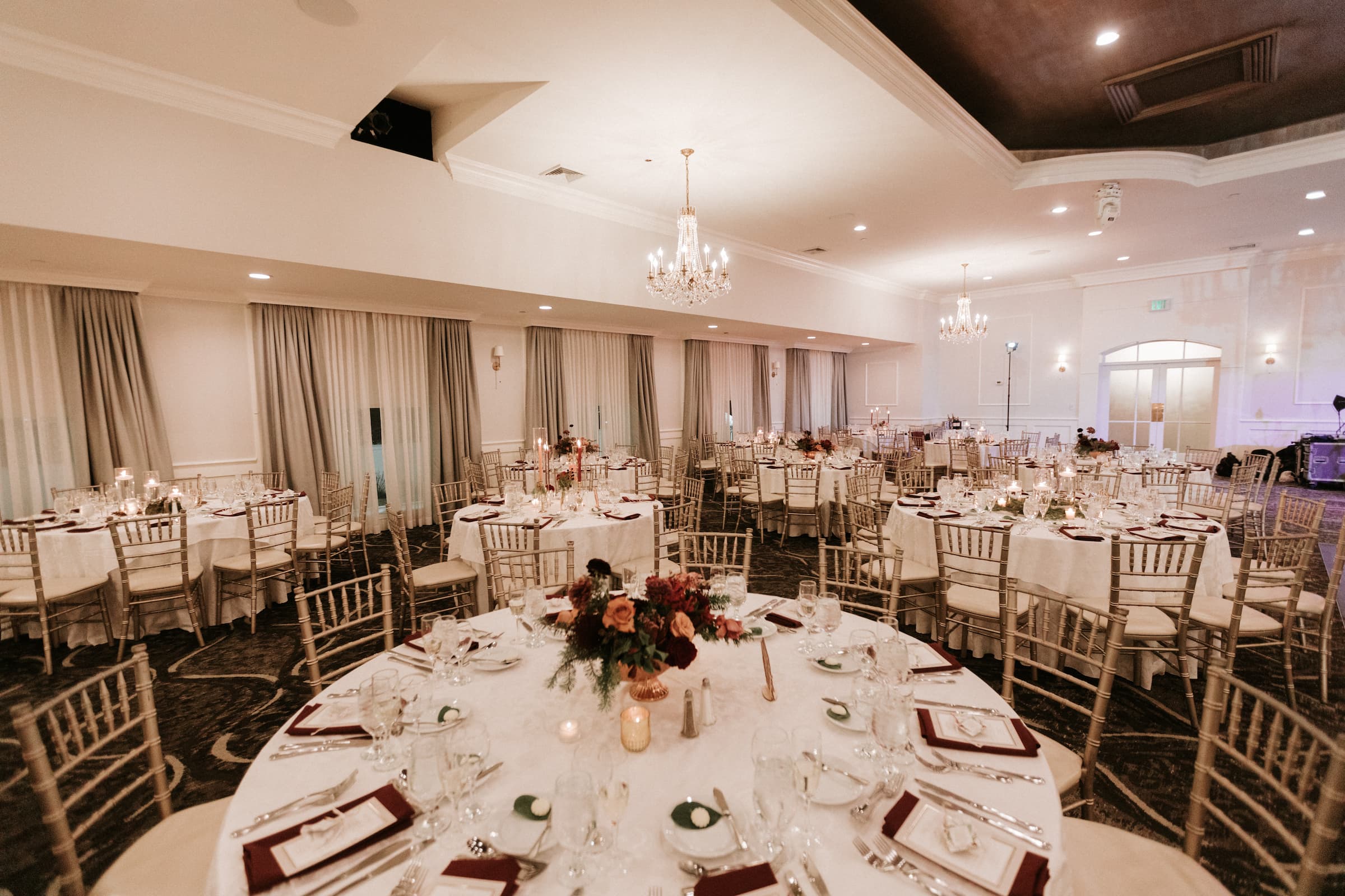 A wideshot of a ballroom with the tables set and chandeliers.