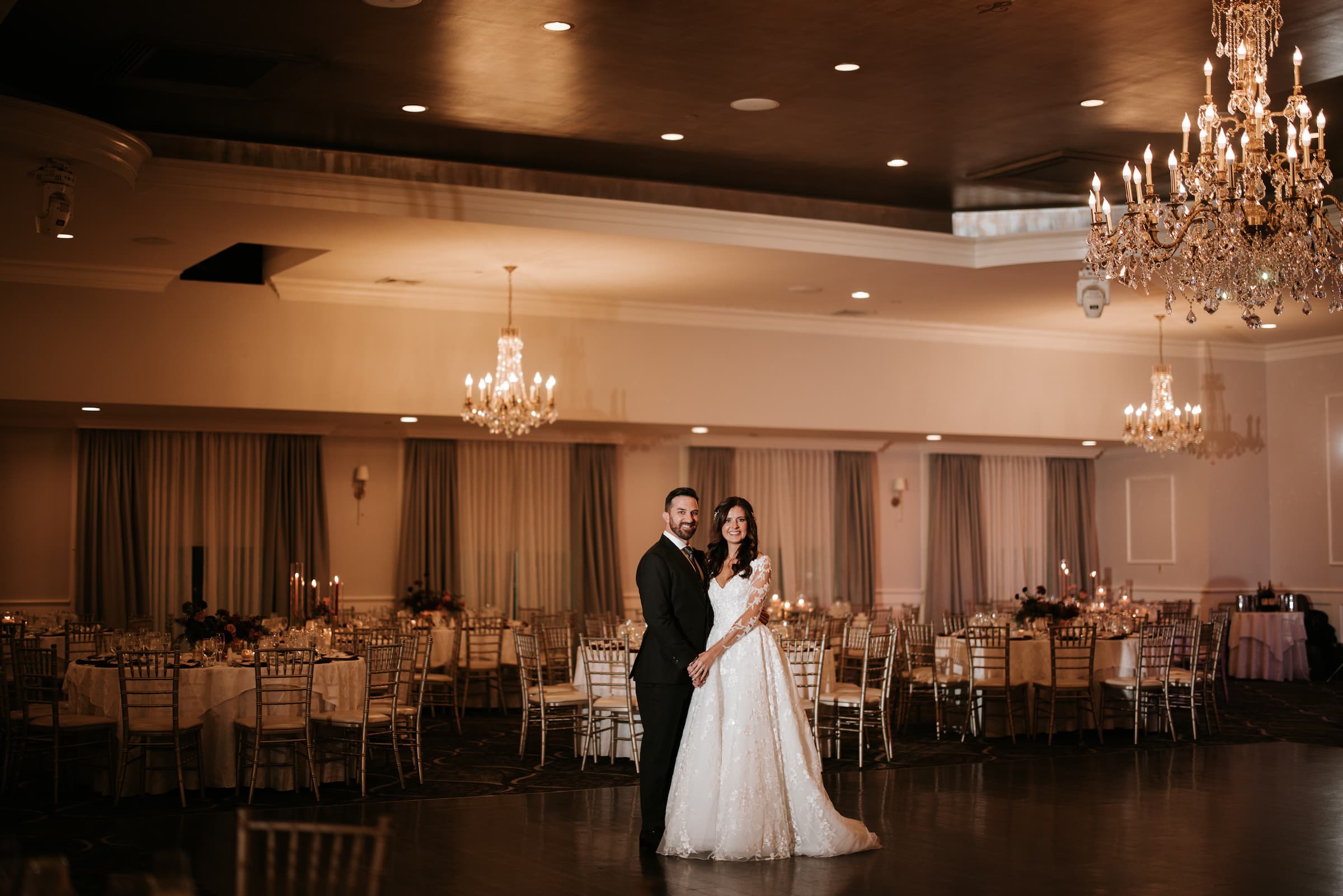 A bride and groom on the dance floor in an otherwise empty ballroom with a chandelier.