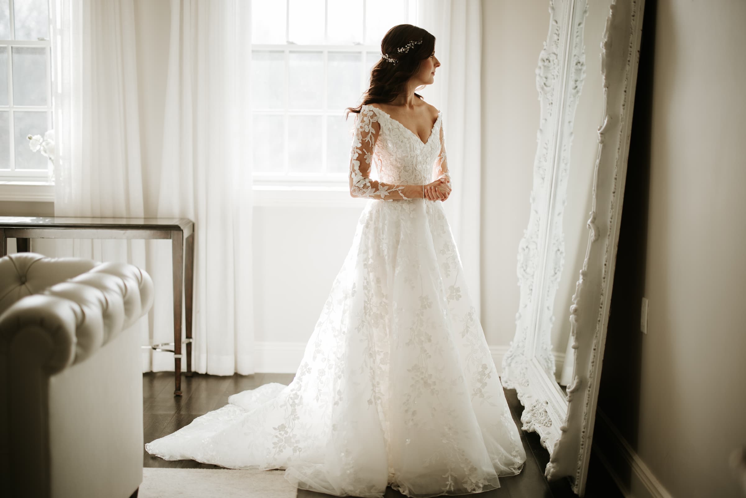 A silhouette side shot of a bride admiring her gown in the mirror with her hands folded at her waist.