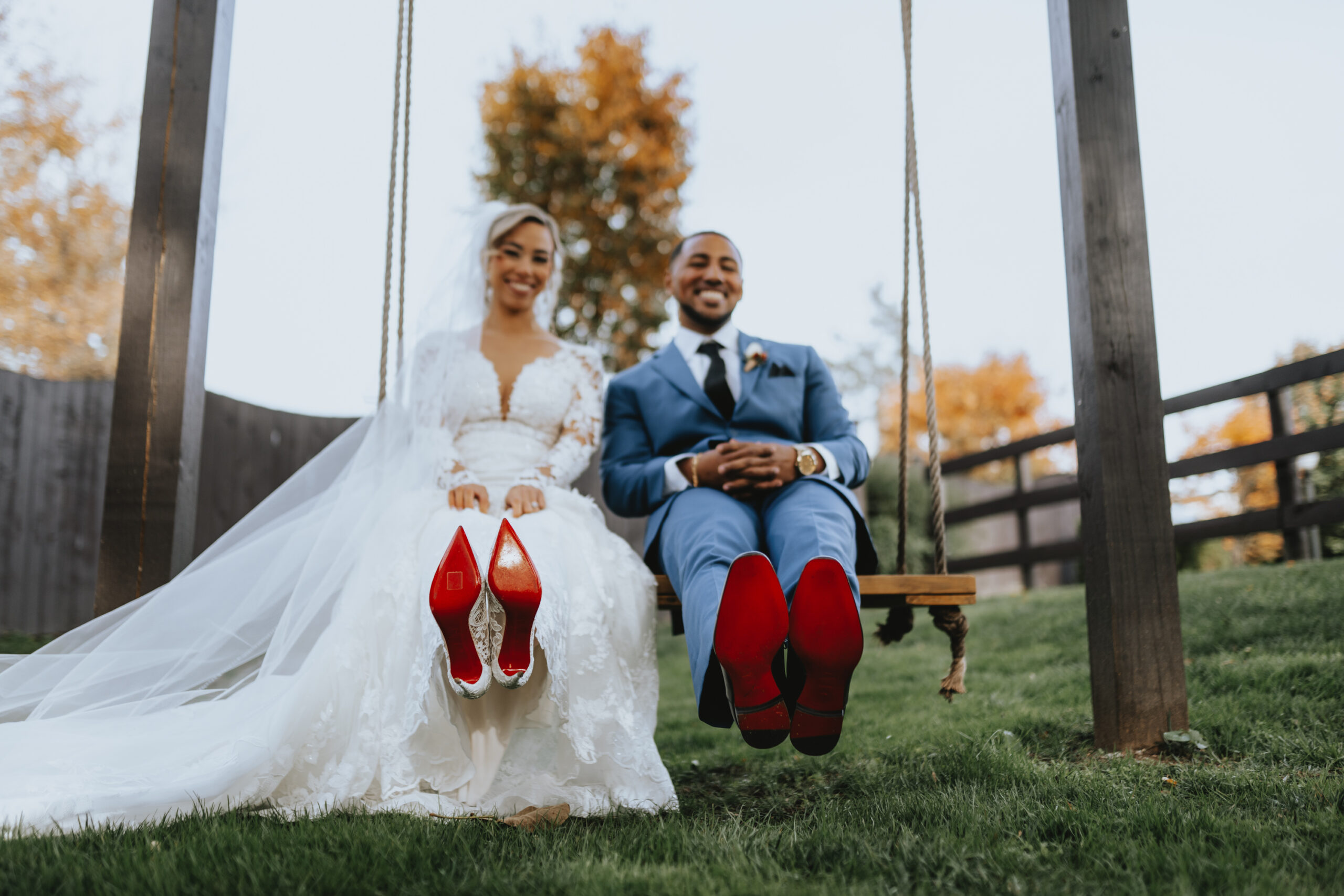 The bride and groom sit on a swing and show off the red bottom of their shoes at their Hamilton Manor wedding.