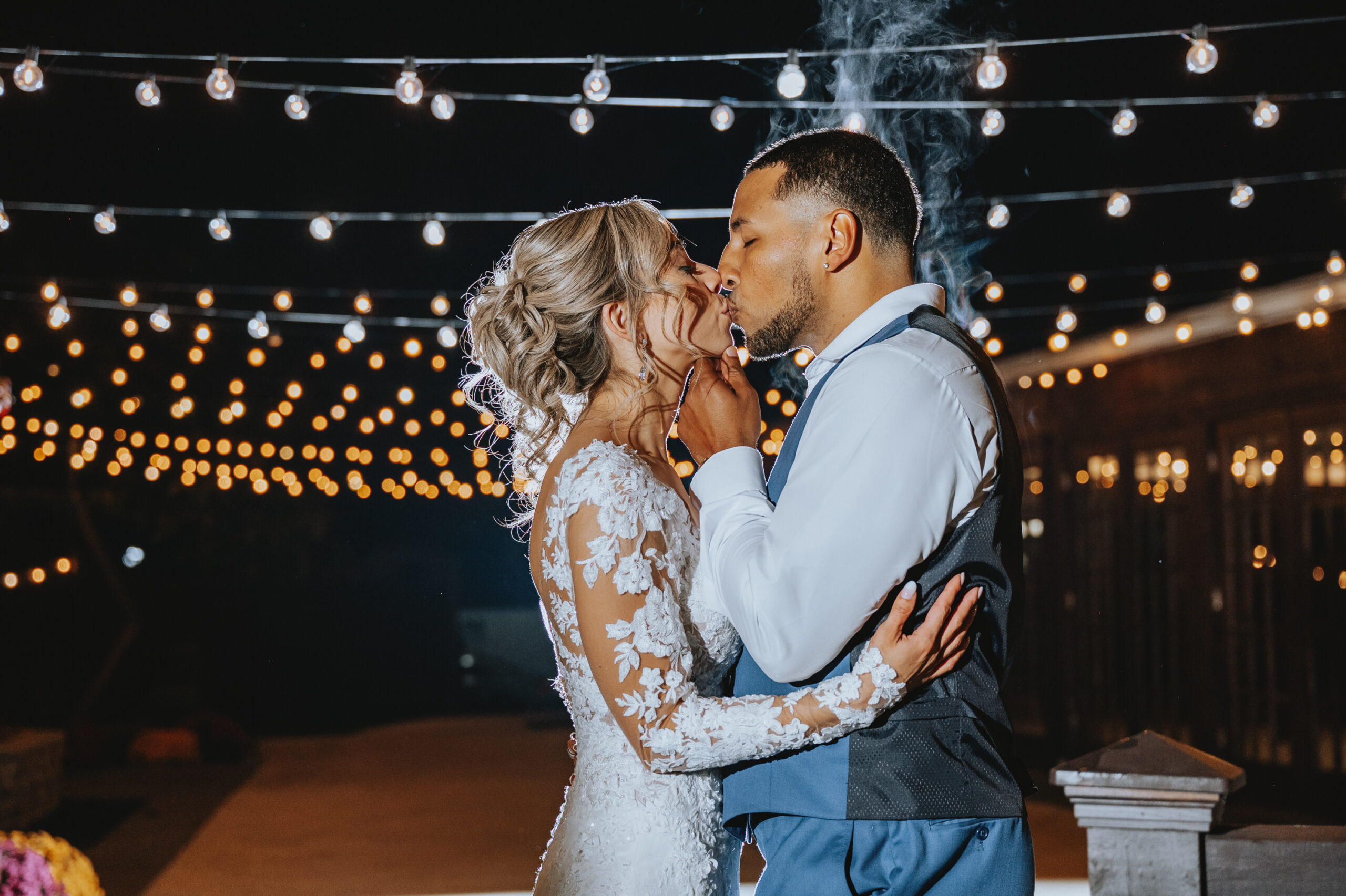 The bride and groom kiss outside under sting lights at their Hamilton Manor wedding.