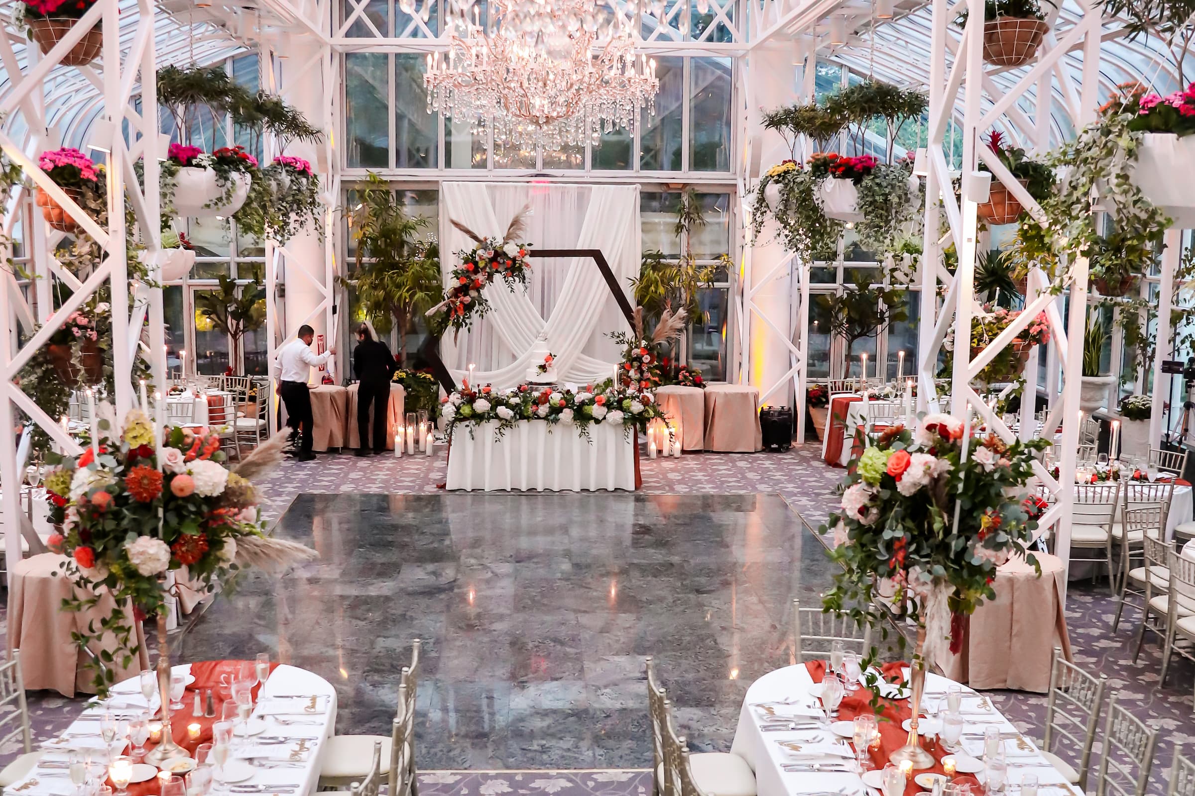 The reception room at the Madison Hotel in Morristown features a large crystal chandelier, floor-to-ceiling glass winders, and hanging plants and flowers.