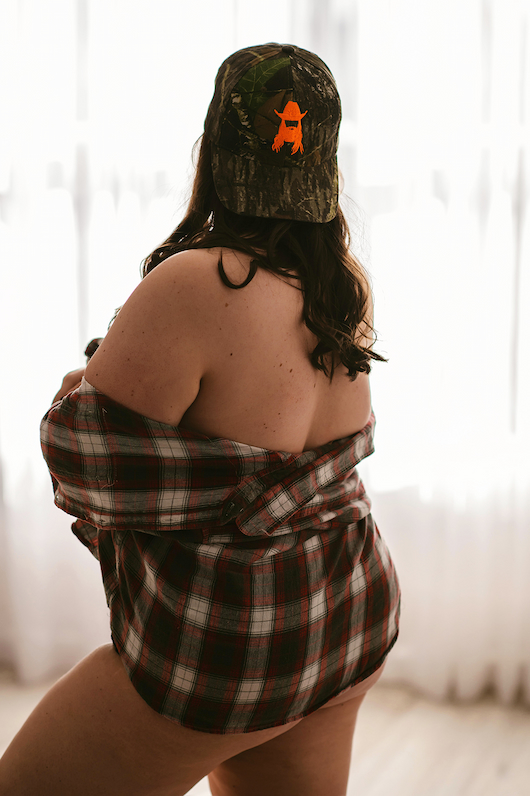 A woman donning a plaid shirt and a backwards baseball cap during her NJ boudoir photoshoot.