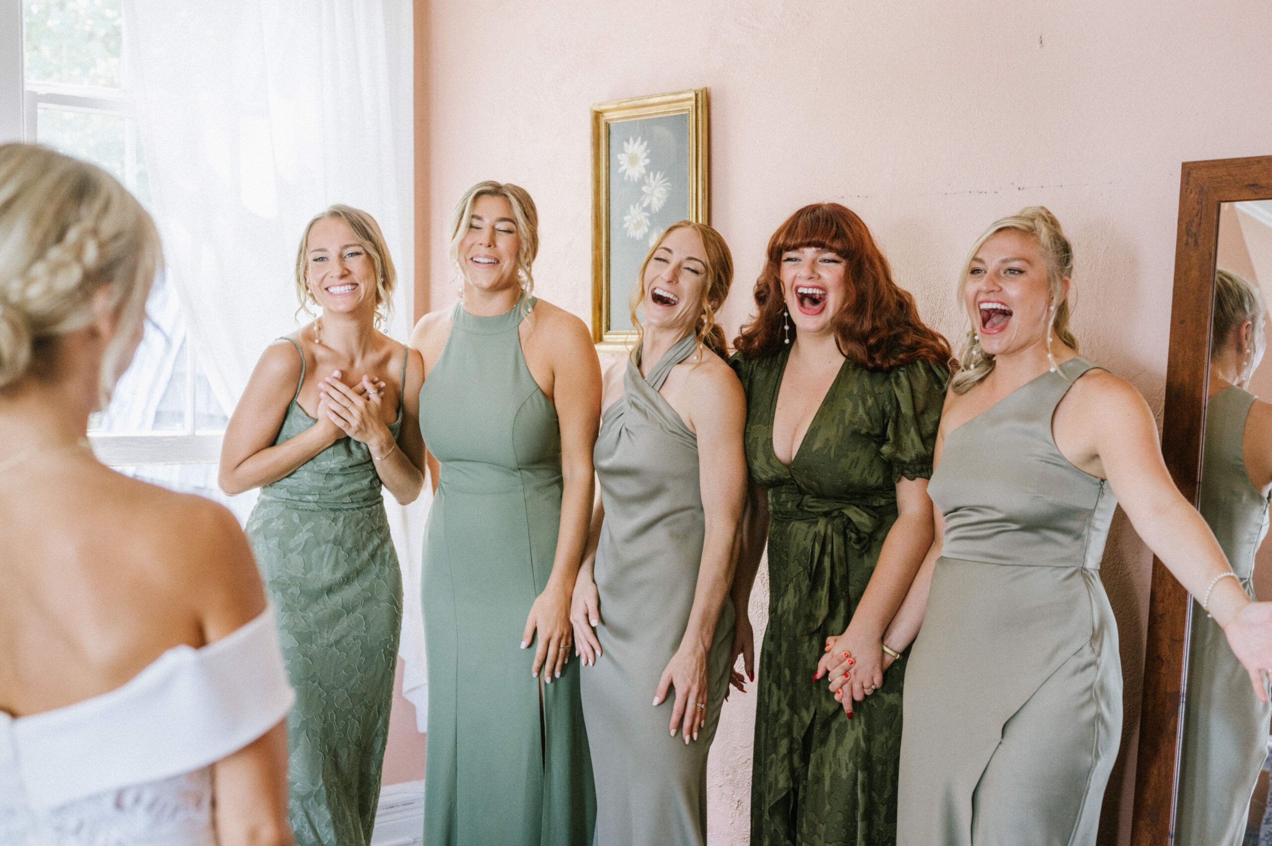 The bridesmaids, in various shades of green, react to seeing the bride in her dress at the Water Witch Club.