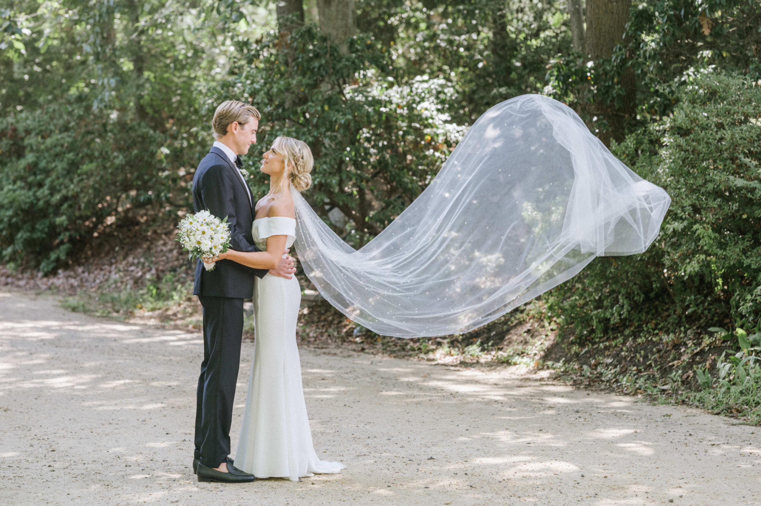 The couple poses with the bride's veil flying in the wind at the Water Witch Club.