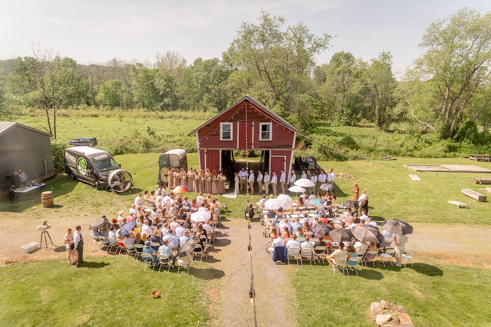 An aerial shot of the red barn and people in seats at the ceremony of Leah and Zeppy's Glenmoore Farm wedding.