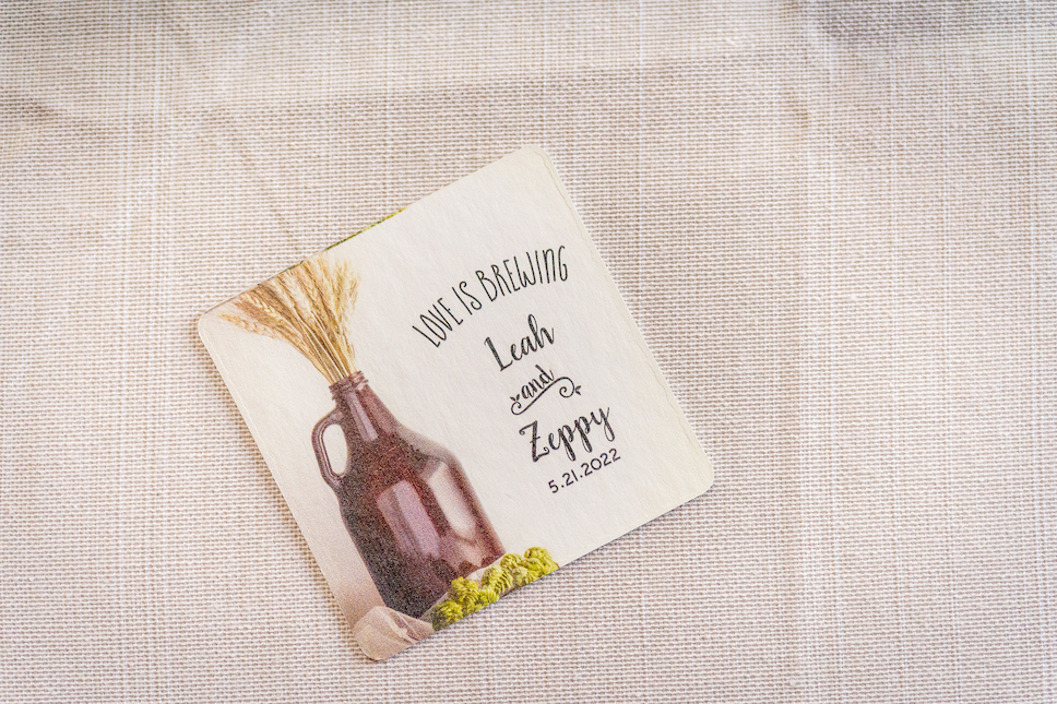 A coaster from their Glenmoore Farm wedding that reads Love is Brewing, Leah and Zeppy, 5.21.2022. 