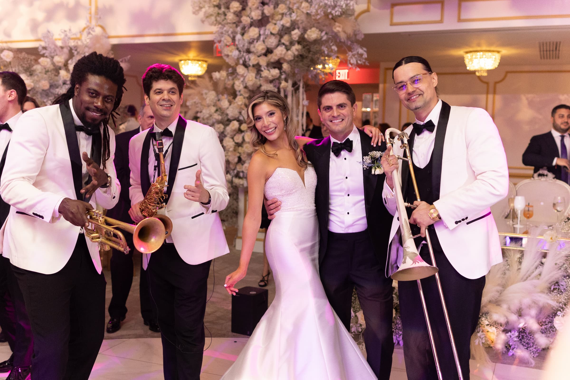 The bride and groom post with three members of their band: the trumpeter, saxophonist and trombonist wearing white suit jackets.