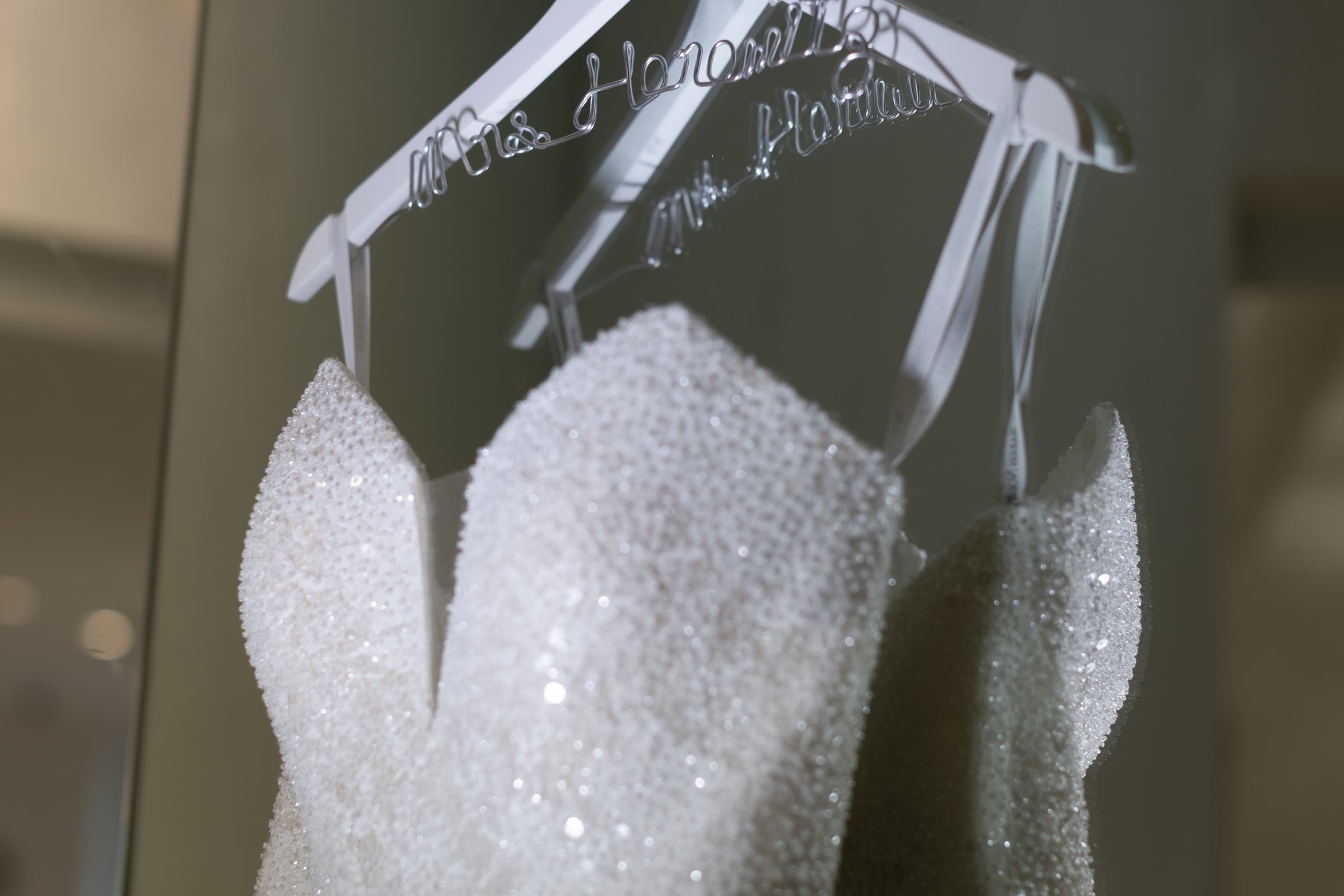 A sparkling wedding dress hangs on a personalized hanger with the bride's new last name.