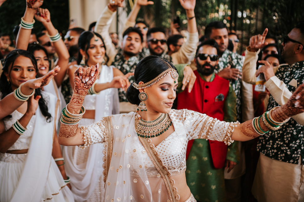 The bride, wearing white with green and gold accessories in accordance with her Indian heritage, dances during the bridal Baraat at Westmount Country Club.